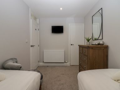 A bedroom with two beds a wooden dresser a wall-mounted TV and two doors at Garden Cottage No 1 in Keswick