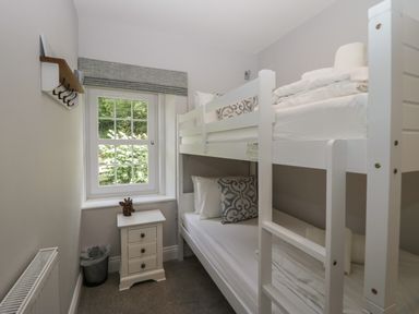 A bedroom with white bunk beds a small side table with drawers a window and a wall-mounted coat rack at Garden Cottage No 1 in Keswick