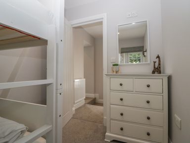 A bedroom with a white bunk bed a white chest of drawers with a mirror and two giraffe figurines at Garden Cottage No 1 in Keswick