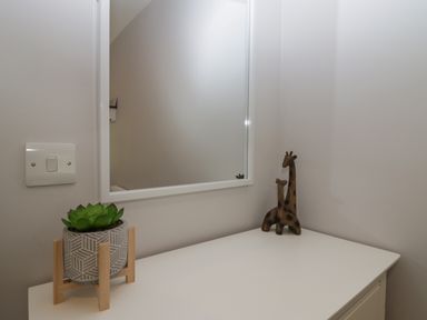 A white table with a small green plant in a pot and two wooden giraffe figurines in front of a wall mirror at Garden Cottage No 1 in Keswick