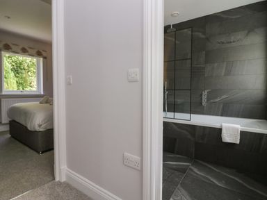 A bathroom with a bathtub and dark tiles next to a bedroom with a bed and a window at Garden Cottage No 1 in Keswick