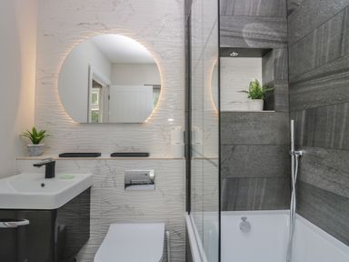 A bathroom with a sink a toilet a round mirror and a bathtub with dark tiles at Garden Cottage No 1 in Keswick