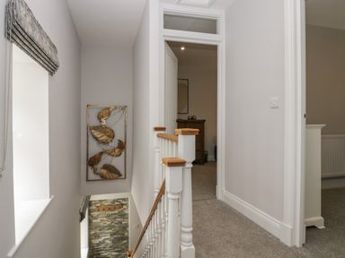 A carpeted hallway with white walls and wooden bannister leading to an open door and window at Garden Cottage No 1 in Keswick