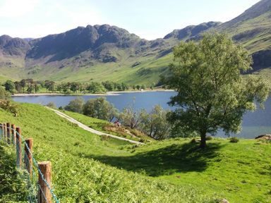 A lake surrounded by green hills trees and a walking path at Garden Cottage No 1 in Keswick