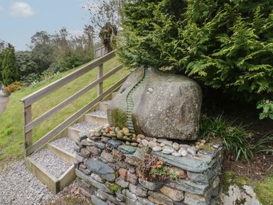 A stone sculpture on a stone wall next to wooden stairs with gravel on the steps at Pod No 5 in Keswick