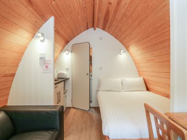 A small room with wooden ceiling walls a bed a kitchenette black sofa and a wooden chair at Pod No 5 in Keswick