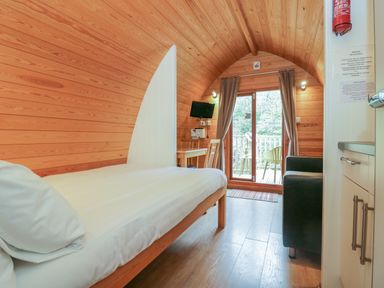 A bedroom with a single bed a black armchair a small table with a chair a wall-mounted tv and glass doors leading to a balcony at Pod No 5 in Keswick