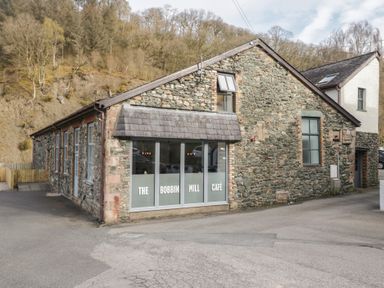 A stone building with large windows and a cafe sign at The Bobbin Mill in Keswick