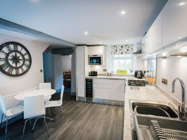 A kitchen with white cabinets a round white table with four chairs and a large wall clock at Greta House in Keswick
