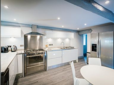 A modern kitchen with stainless steel oven and refrigerator white cabinets and a round dining table at Greta House in Keswick