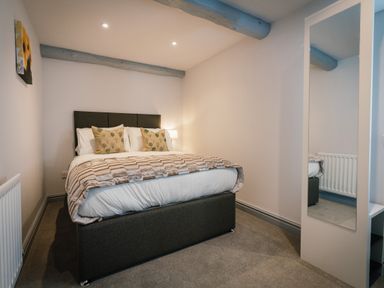 A bedroom with a double bed two pillows a lamp and a tall mirror at Greta House in Keswick