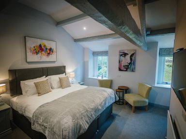 A bedroom with a double bed and two chairs near windows at Greta House in Keswick