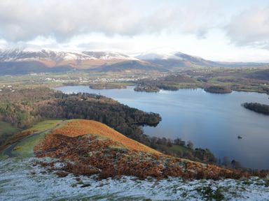 A view of a lake surrounded by trees and fields with snow capped hills in the background at Greta House in Keswick