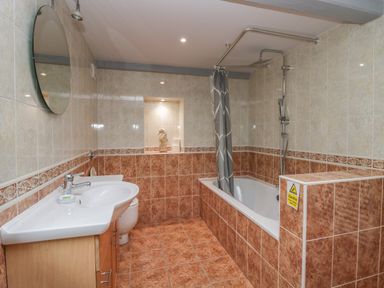 A bathroom with a bathtub shower combination a sink with a mirror above and a toilet at Greta House Keswick