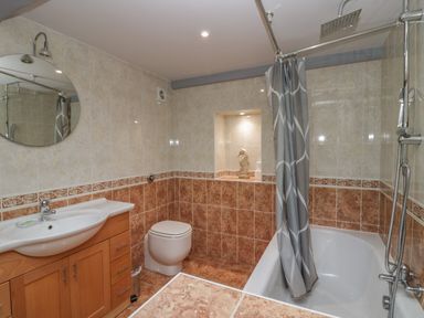 A bathroom with a sink and wooden cabinet a toilet a bathtub with a shower and curtain and a decorative seahorse statue in a tiled niche at Greta House in Keswick