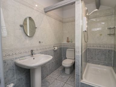 A bathroom with a pedestal sink a round mirror a toilet and a shower at Greta House in Keswick