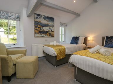 A bedroom with two single beds a chair with an ottoman a lamp and abstract wall art at Greta House in Keswick