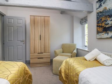 A bedroom with two beds with yellow covers a wardrobe an armchair and a window at Greta House Keswick