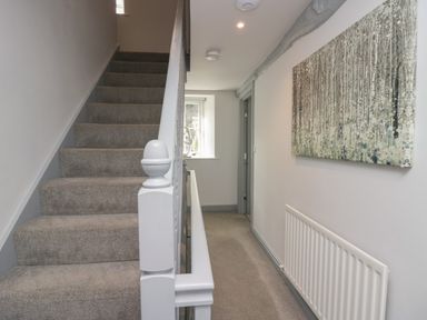 A hallway with carpeted stairs a radiator and a painting on the wall at Greta House in Keswick