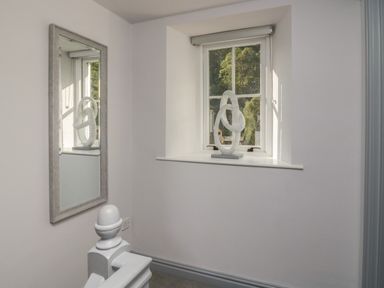 A window with a sculpture on the sill and a mirror reflecting the sculpture in a hallway at Greta House in Keswick