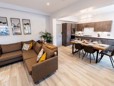 An open-plan living room and kitchen with a brown sectional sofa and a wooden dining table at Briery House in Keswick