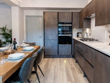 A kitchen with wooden dining table set with plates and glasses and dark cabinets with built in ovens at Briery House in Keswick