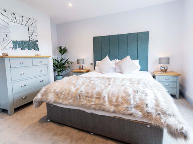 A bedroom with a bed with fur blanket two bedside tables with lamps a chest of drawers a plant and a decorative mirror at Briery House in Keswick