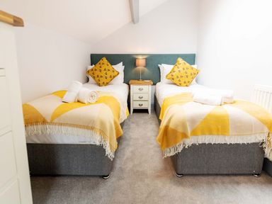 A bedroom with two single beds yellow blankets and pillows and a nightstand with a lamp at Briery House in Keswick