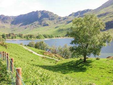 A lake with surrounding trees and grassy hills with mountains in the background at Briery House Keswick