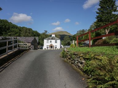A paved road leading to a white house with trees and hills in the background at Briery House in Keswick