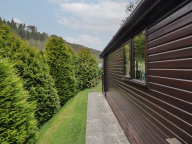 A side view of a brown cabin with a paved pathway and green trees along the side at Canadian Cabin No 38 in Keswick