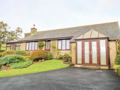 A single-story house with stone walls and a slate roof with a paved driveway and shrubs at Pinegarth in Catton near Allendale