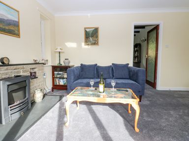 A living room with a blue sofa and a glass coffee table with a bottle and glasses at Pinegarth in Catton near Allendale