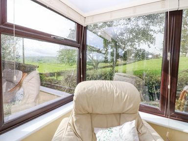A cream-colored armchair with a pillow in front of large windows showing a green outdoor landscape at Pinegarth in Catton near Allendale