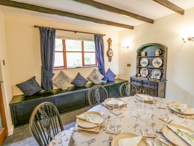 A dining room with a table set for six and a window seat with cushions at Pinegarth in Catton near Allendale