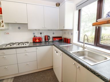 A kitchen with white cabinets a gas stove a sink a window and red kitchen appliances at Pinegarth in Catton near Allendale