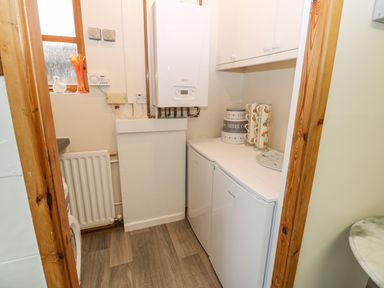 A utility room with a boiler radiator washing machine and cupboards at Pinegarth Catton near Allendale