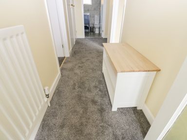 A hallway with gray carpet a white radiator on the left and a white wooden console table on the right at Pinegarth Catton near Allendale