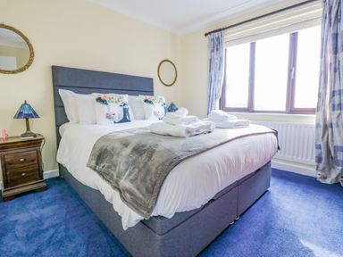 A bedroom with a double bed with animal print pillows bedside table with lamp and a large window at Pinegarth in Catton near Allendale