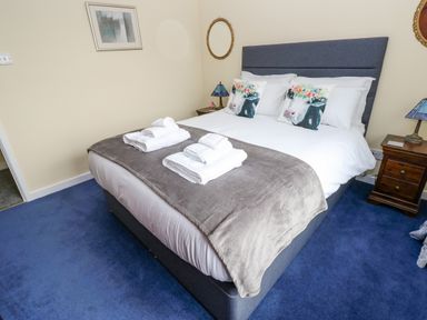 A bedroom with a bed with white linens and two pillows with cow faces on a blue carpet at Pinegarth in Catton near Allendale