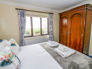 A bedroom with a bed made with white linens and floral pillows towels on the bed a large wooden wardrobe and a window with patterned curtains at Pinegarth Catton near Allendale