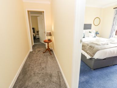 A hallway with a small wooden table and lamp leading to bedrooms with beds and bedside tables at Pinegarth in Catton near Allendale
