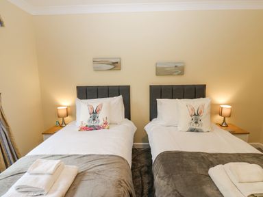 A bedroom with two single beds each with a grey headboard white bedding grey blankets and rabbit themed pillows with bedside tables and lamps at Pinegarth Catton near Allendale