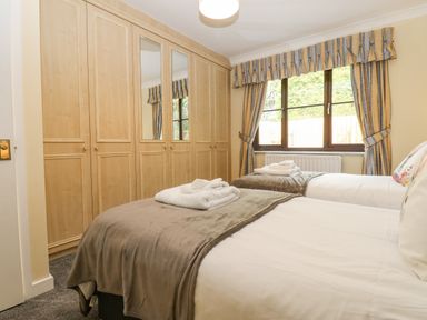A bedroom with two single beds folded towels wooden wardrobes and a window with striped curtains at Pinegarth Catton near Allendale