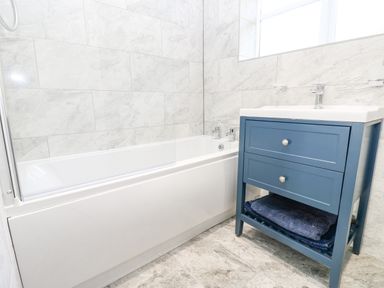 A bathroom with a white bathtub and a blue vanity unit with towels underneath at Pinegarth in Catton near Allendale