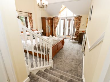 A bedroom with a wooden bed, wardrobe, chair, and French doors leading outside at Pinegarth Catton near Allendale