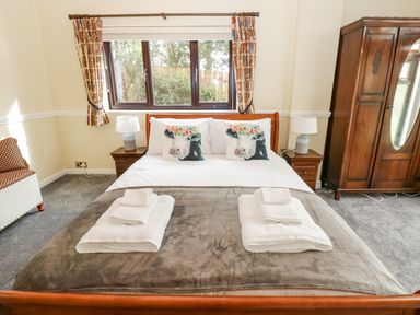 A bedroom with a double bed with white pillows and blankets two nightstands with lamps a wooden wardrobe and a small sofa at Pinegarth in Catton near Allendale