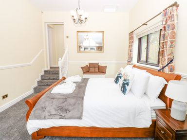A bedroom with a wooden bed a side table a lamp a window with curtains a bench with cushions and stairs in the background at Pinegarth in Catton near Allendale