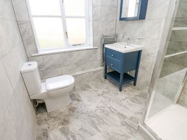 A bathroom with a toilet a blue vanity with a sink a mirror and a shower at Pinegarth in Catton near Allendale