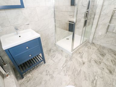 A bathroom with a blue sink cabinet and a glass shower enclosure at Pinegarth in Catton near Allendale